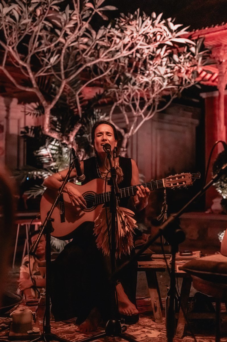 Pao Pamaki singing and playing guitar live under red-lit trees